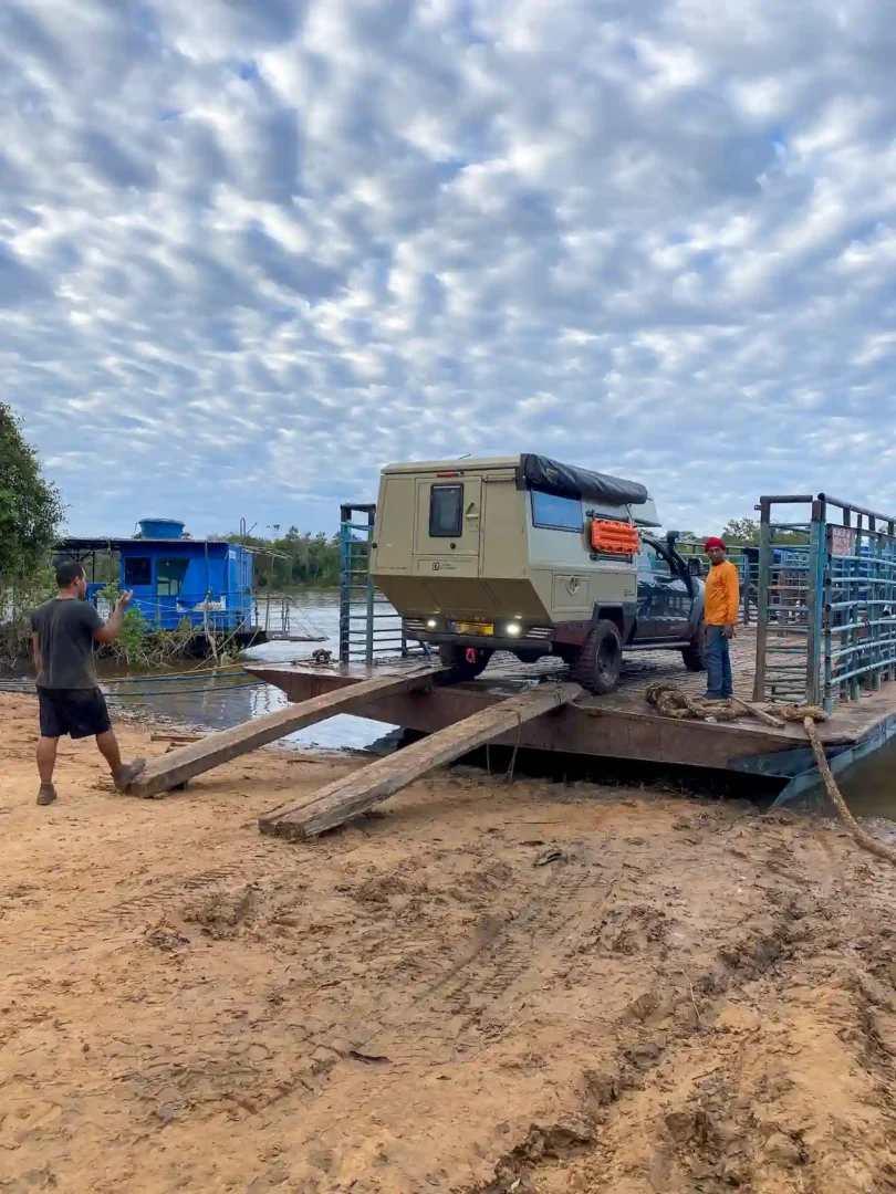 La célula vivienda Pioneer para pick up overland de Land Roamer montada en una pickup que está subiendo a una barca para atravesar un río