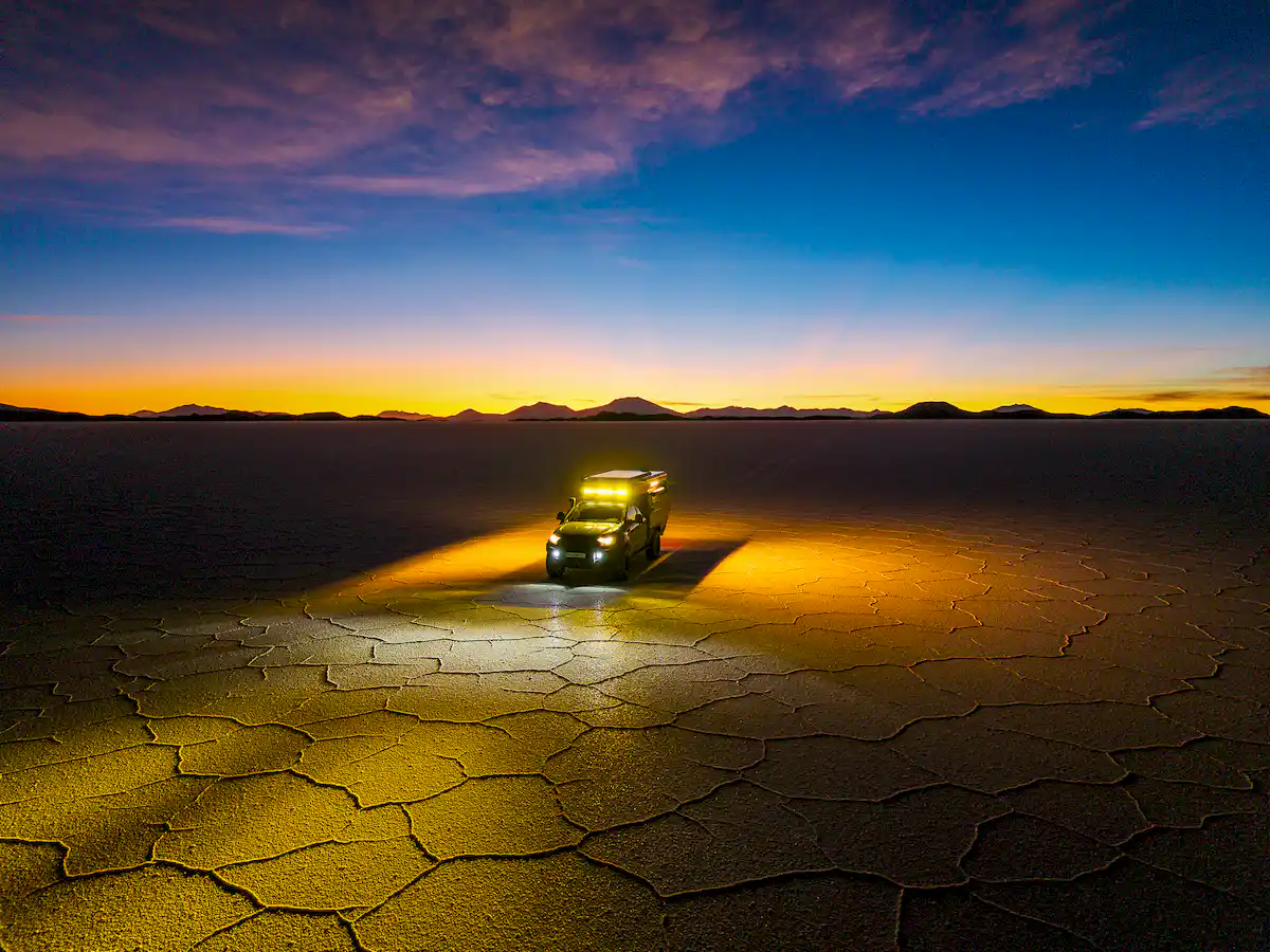 Una pickup overland con la célula vivienda Pioneer de Land Roamer atravesando un río de noche