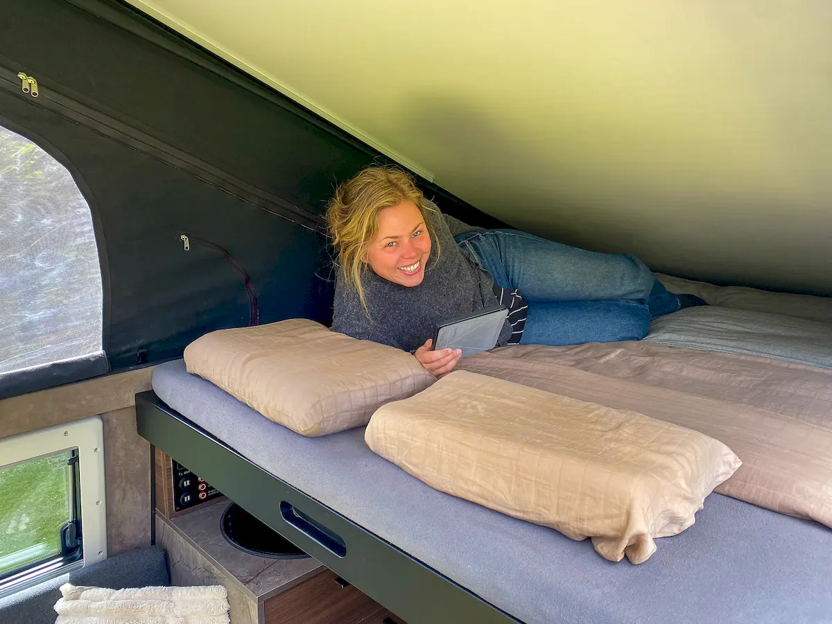 Mujer tumbada en la cama de la confortable célula vivienda Pioneer para pick up overland de Land Roamer
