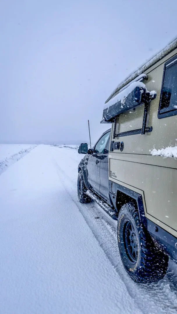 Una pickup 4x4 con la célula vivienda Pioneer de Land Roamer circulando por una carretera nevada