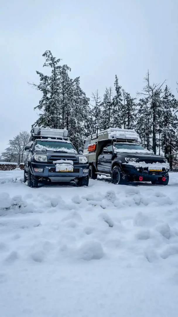 Una pickup 4x4 con la célula vivienda Pioneer de Land Roamer junto a un todoterreno con tienda de techo en la nieve