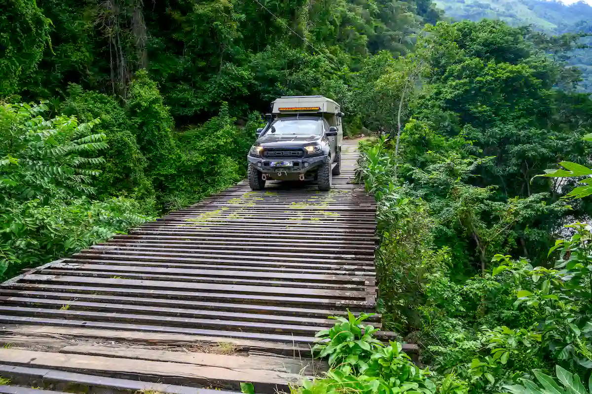Una pickup overland con la célula vivienda Pioneer de Land Roamer atravesando un puente de madera en Sudamérica